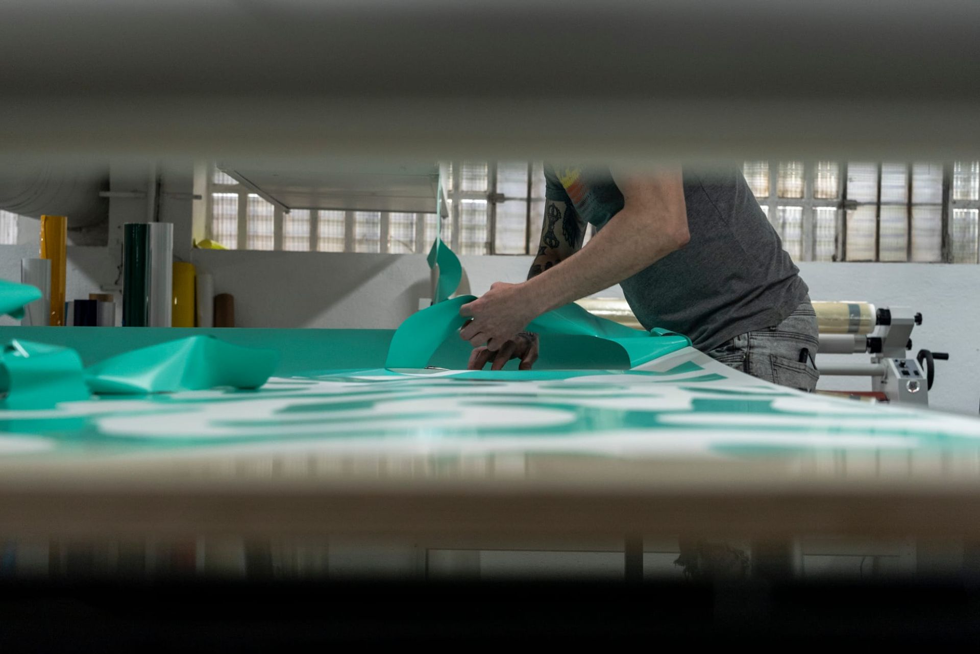 Persona cortando tela verde azulado sobre una mesa en un taller.
