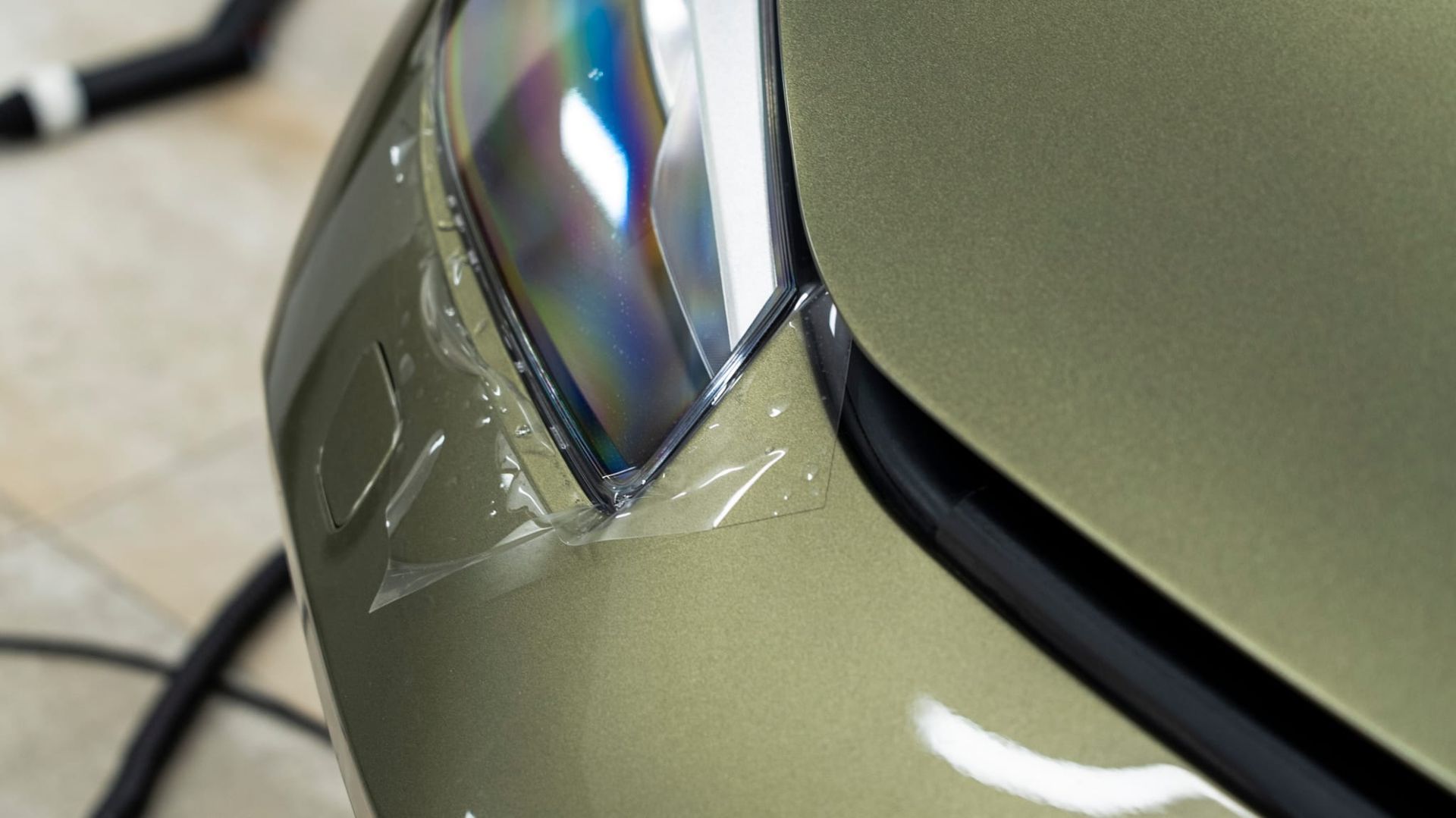 Parachoques de coche con película protectora transparente alrededor de un faro, pintura verde caqui.