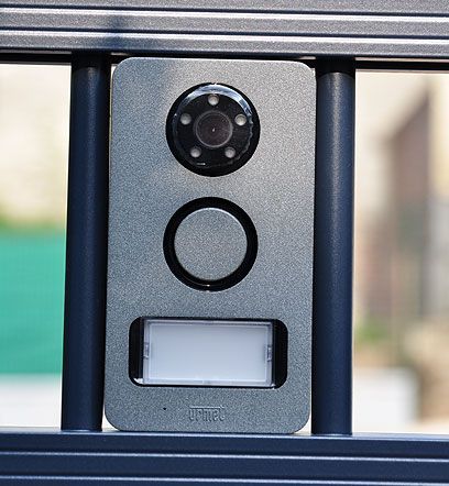 Gros plan sur une sonnette vidéo ou un interphone noir avec capteur et lumière, installé sur un portail métallique