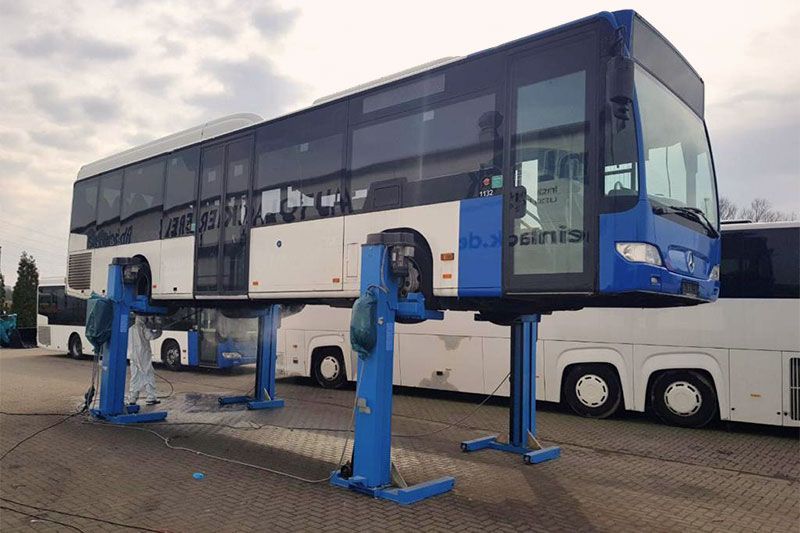 Ein blau-weißer Bus steht auf einer Hebebühne auf einem Parkplatz