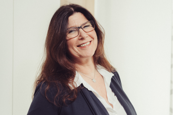 Eine Frau mit Brille und weißem Hemd lächelt in die Kamera