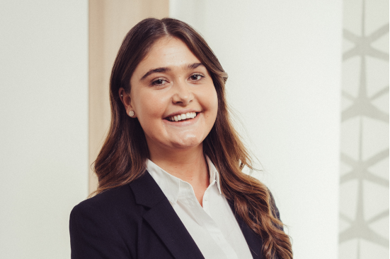 Eine Frau in Anzug und weißem Hemd lächelt in die Kamera.