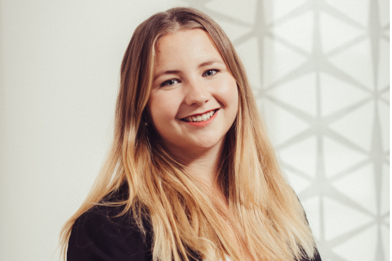 Eine Frau mit langen blonden Haaren lächelt und trägt eine schwarze Jacke