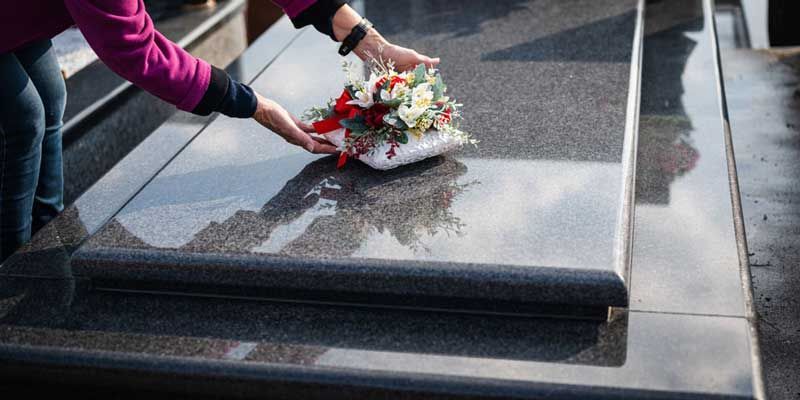 Personne qui pose une gerbe de fleurs sur une pierre tombale