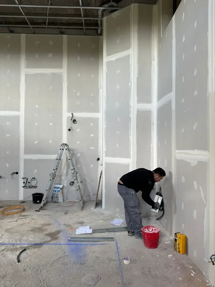 Un hombre está pintando una pared en una habitación con una escalera al fondo.