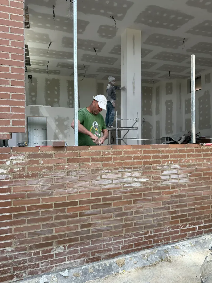 Un hombre con una camisa verde está trabajando en una pared de ladrillos.