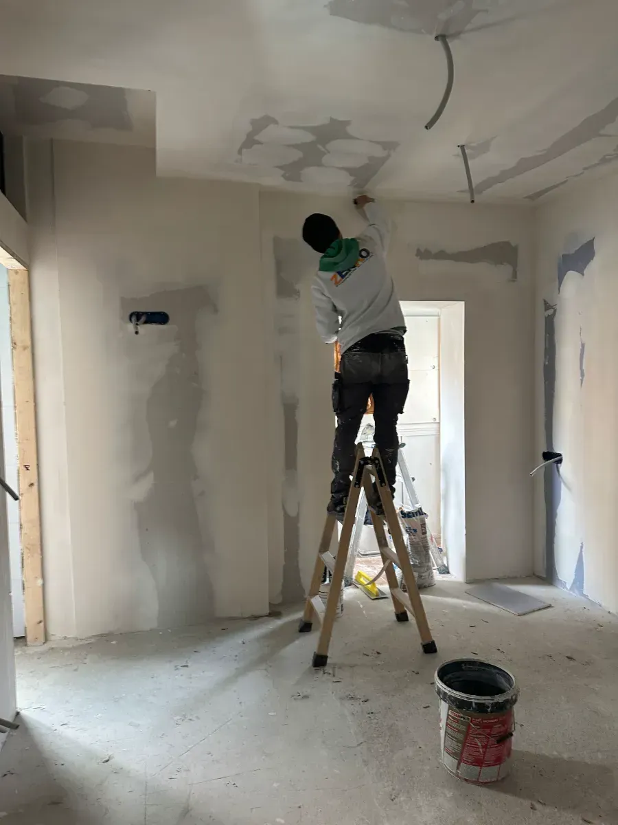 Un hombre está de pie en una escalera pintando una pared.