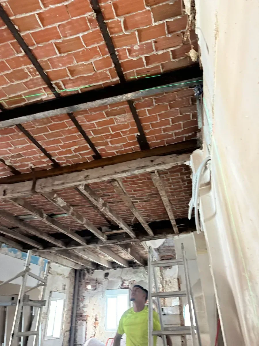 Un hombre está de pie sobre una escalera en una habitación con techo de ladrillo.