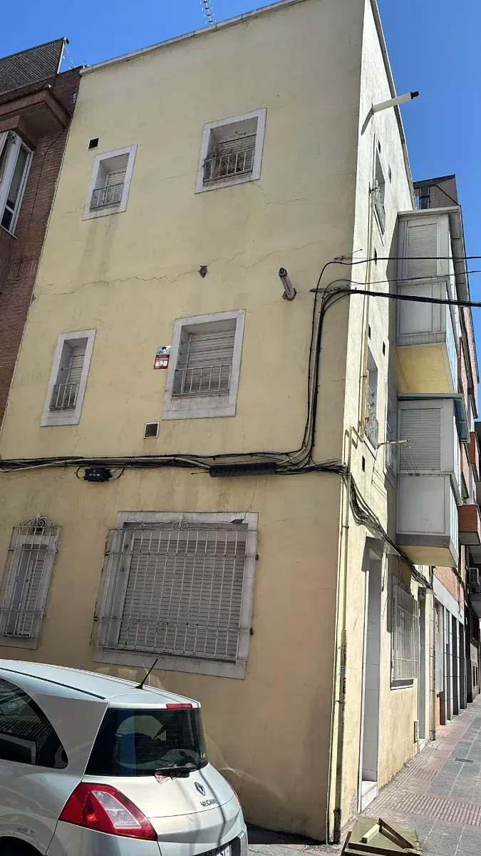 Un coche blanco está aparcado delante de un edificio amarillo.