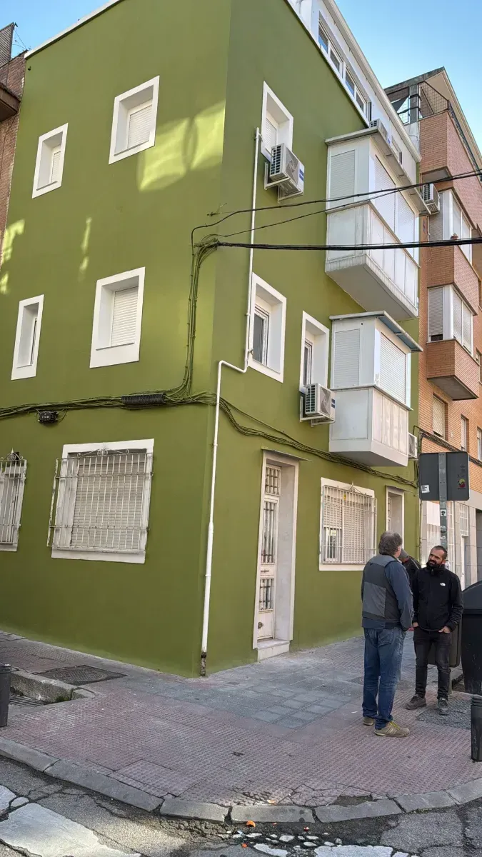 Un grupo de personas está de pie en la acera frente a un edificio verde.