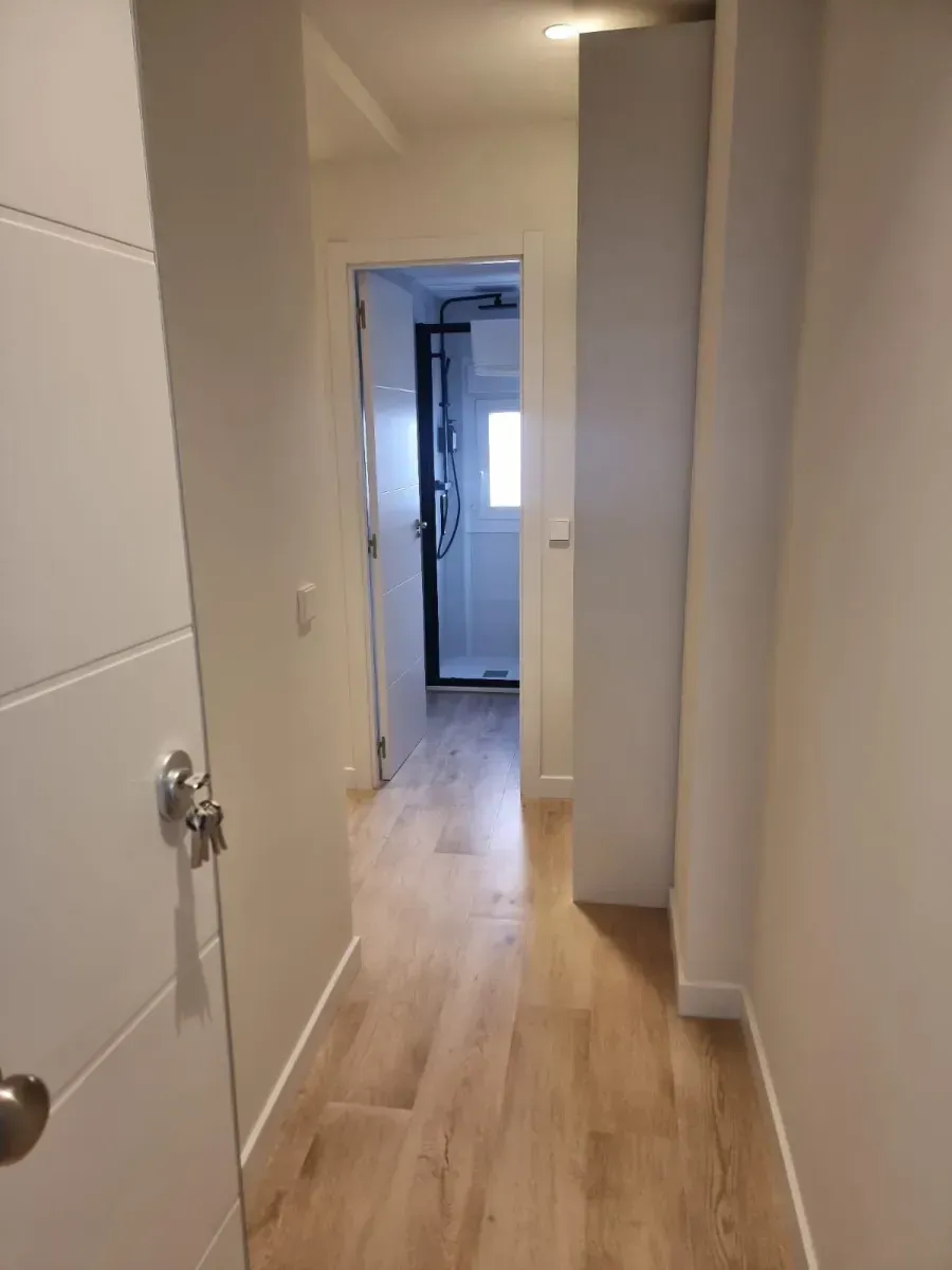 Un pasillo con pisos de madera y paredes blancas que conduce a un baño.