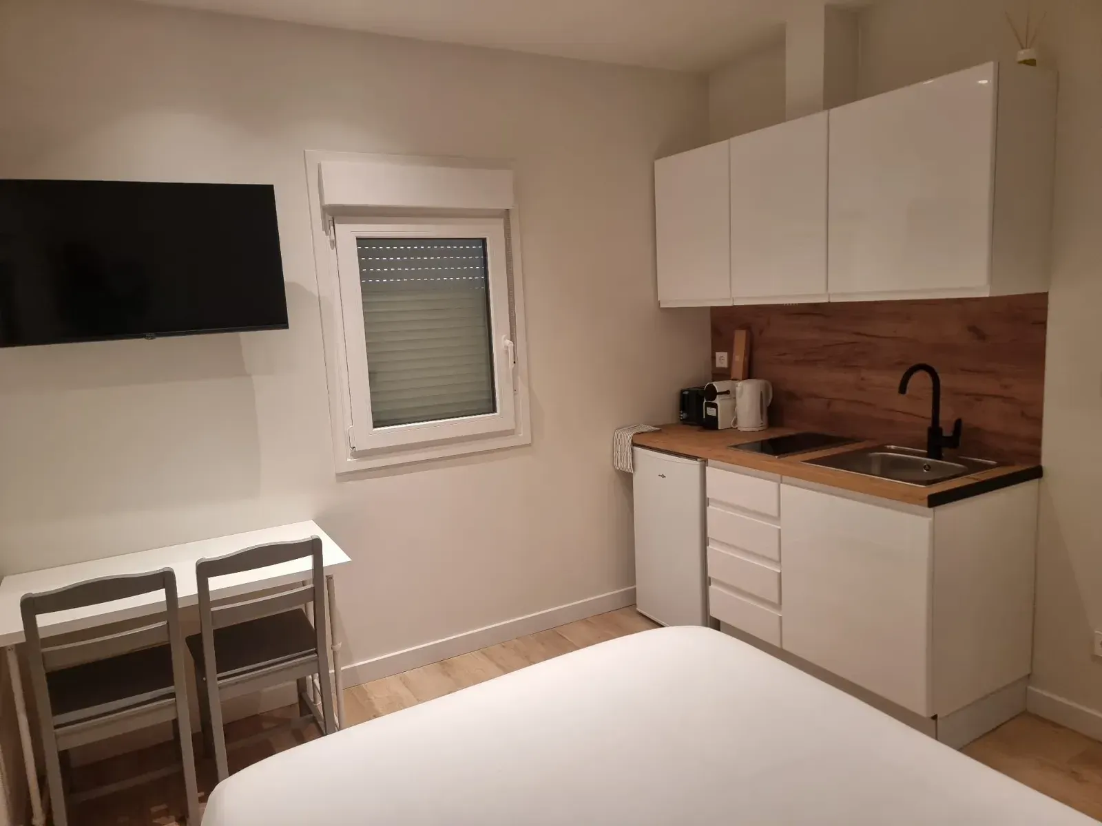 Un dormitorio con cama, escritorio, sillas, televisión y cocina.