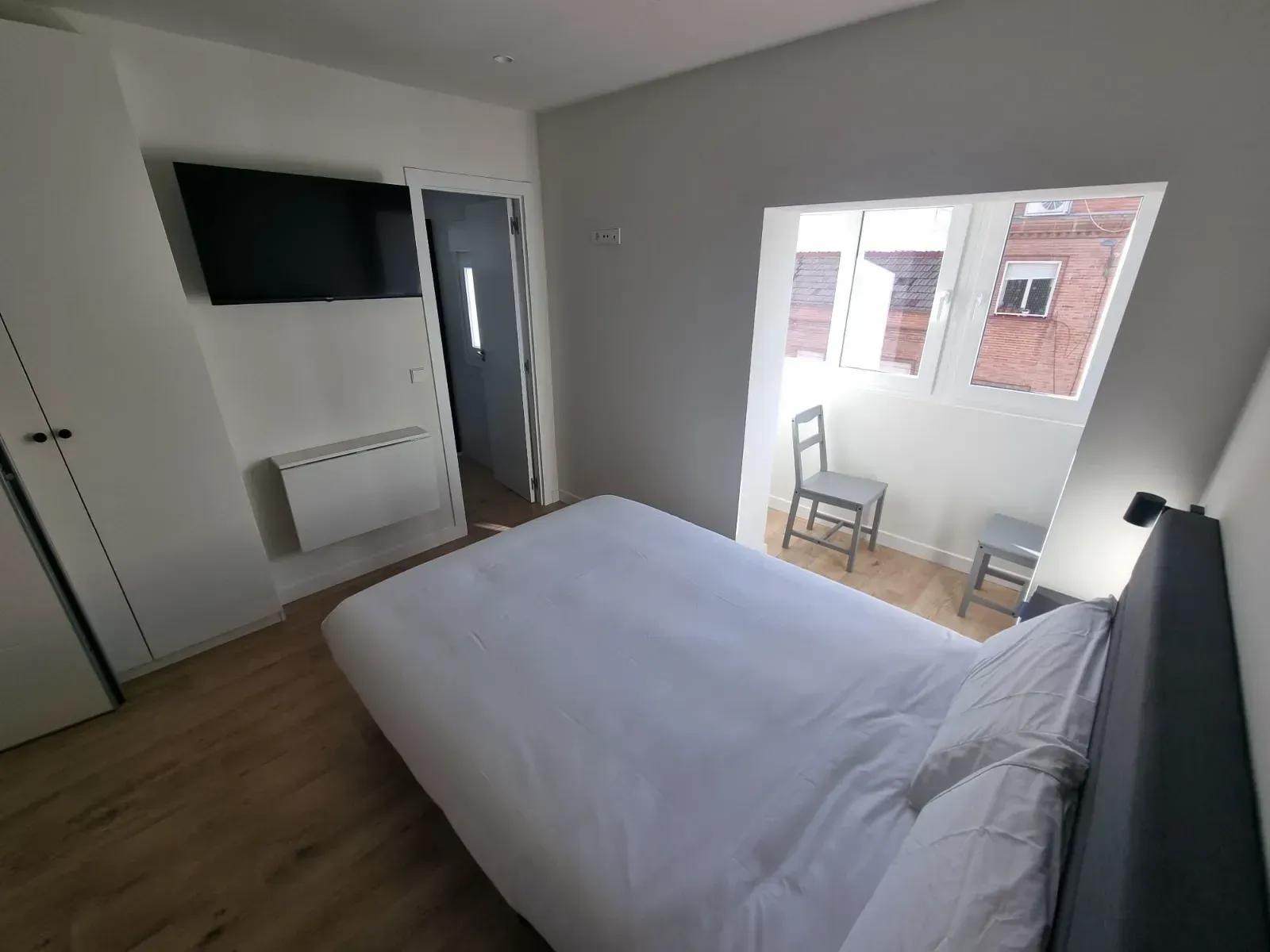Un dormitorio con una cama, sillas, televisión y un balcón.