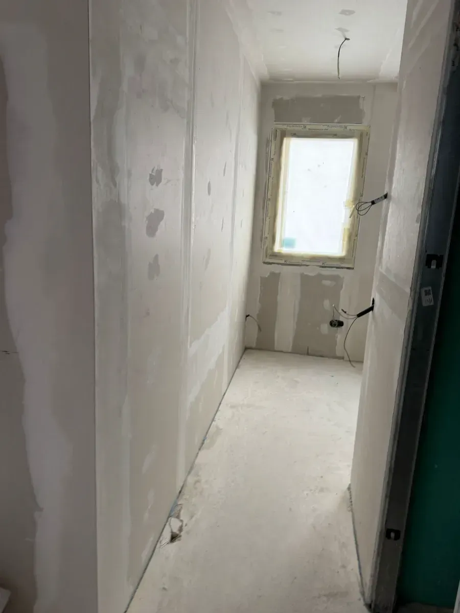 Un largo pasillo con una ventana y una puerta en un edificio en construcción.