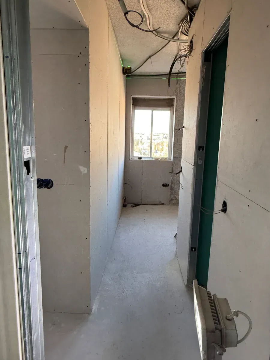 Un largo pasillo con una puerta verde y una ventana.