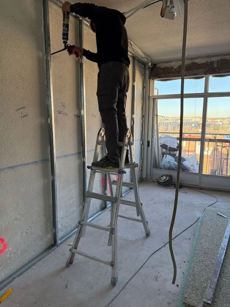 Un hombre está de pie en una escalera trabajando en una pared.