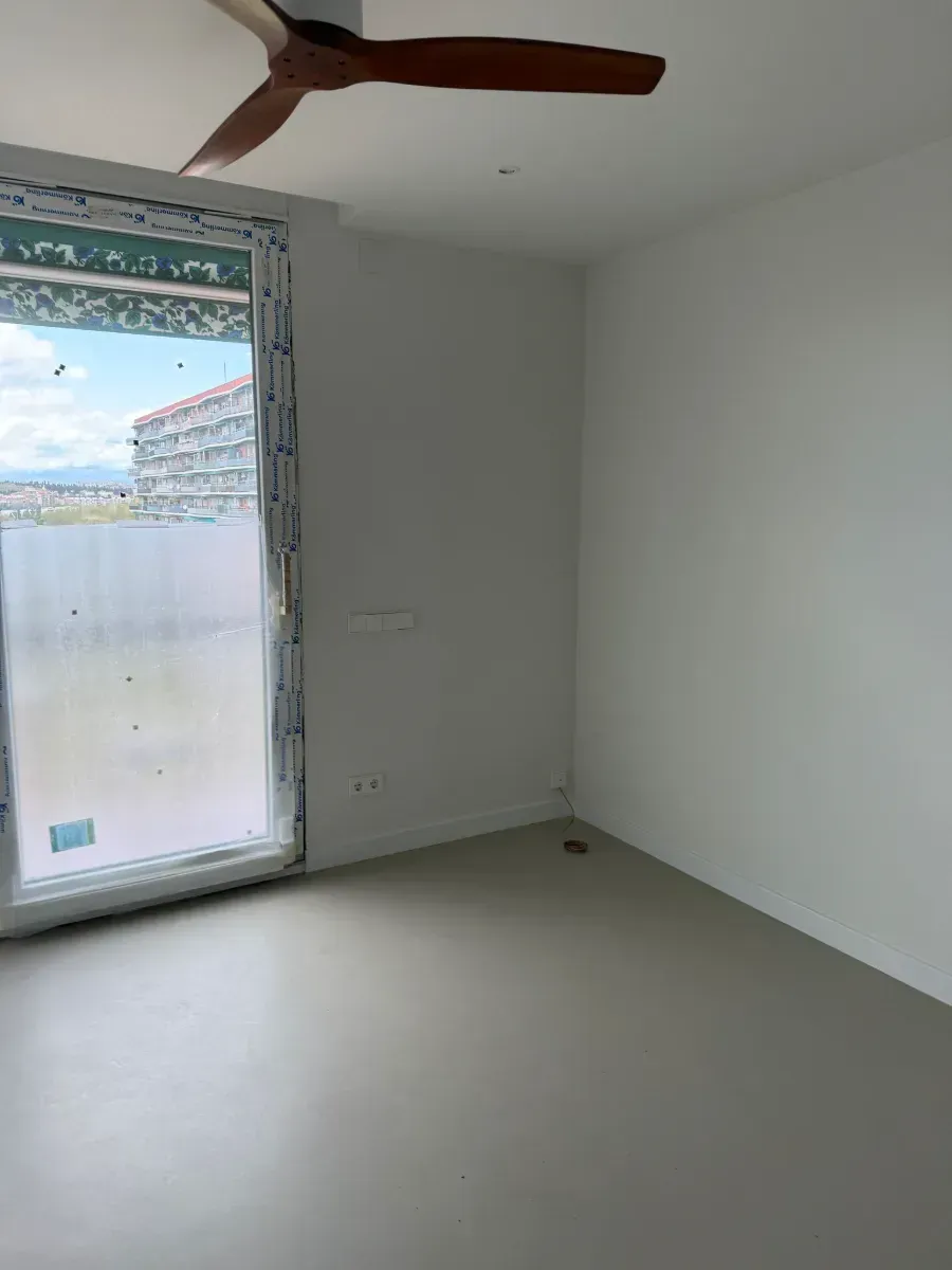 Una habitación vacía con un ventilador de techo y una ventana grande.