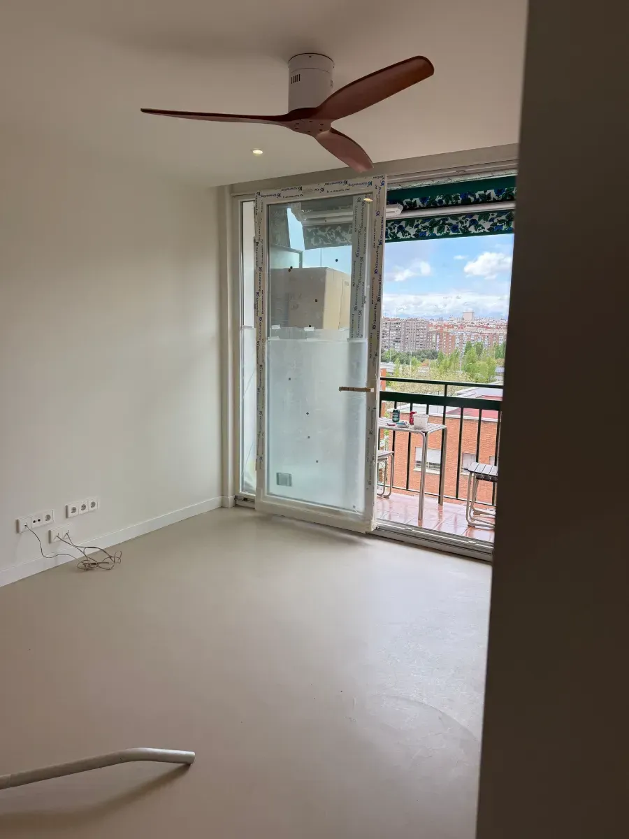 Una habitación vacía con balcón y ventilador de techo.