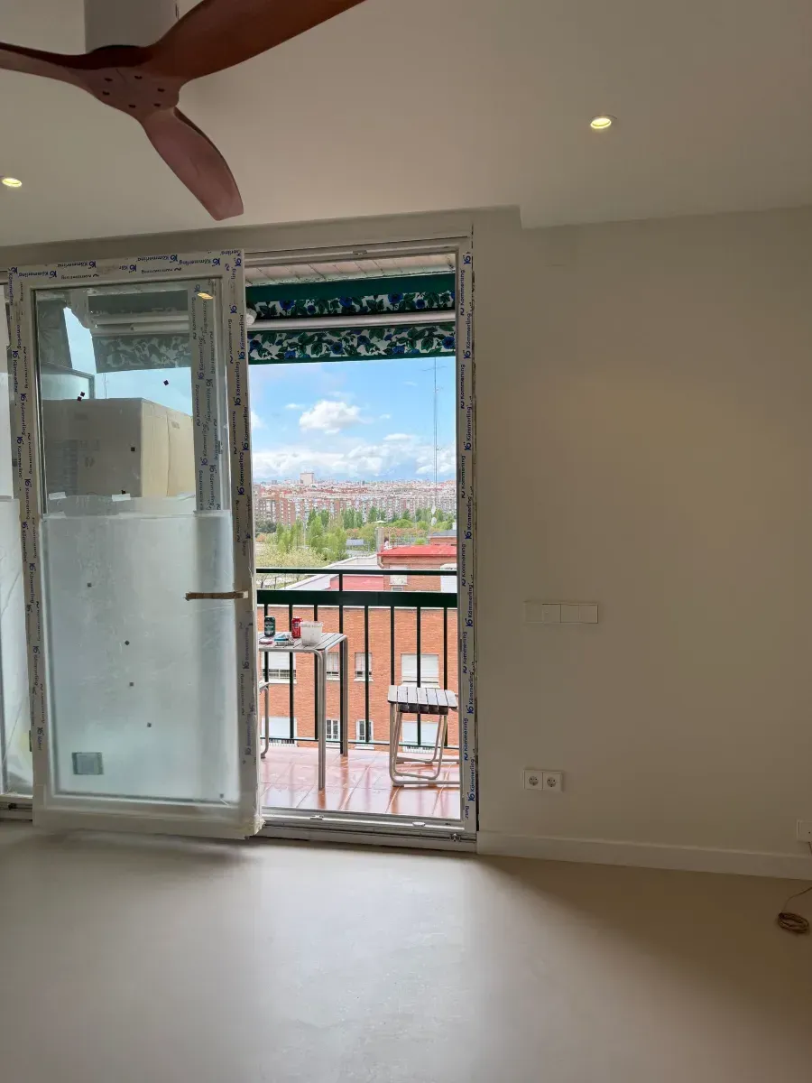 Una habitación vacía con balcón y ventilador de techo.