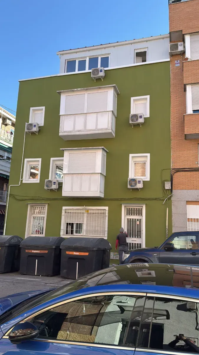 Un coche azul está aparcado delante de un edificio verde.
