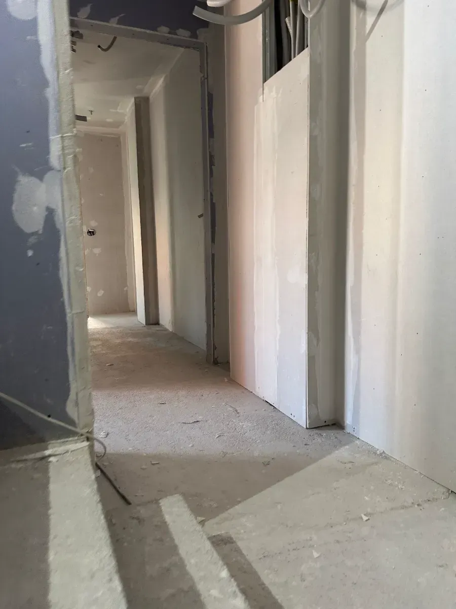 Un largo pasillo con paredes blancas y una puerta en un edificio en construcción.