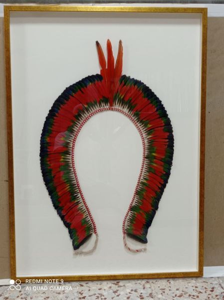 Tocado de plumas enmarcado en rojo, verde y negro sobre fondo blanco.