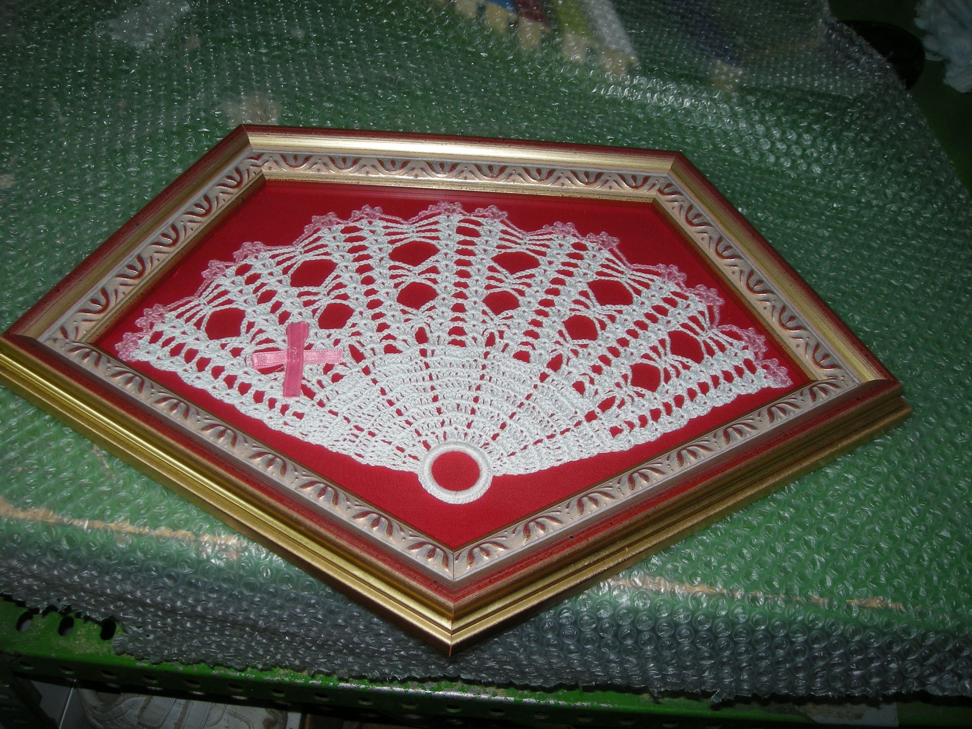 Un abanico de crochet en un marco rojo y dorado.