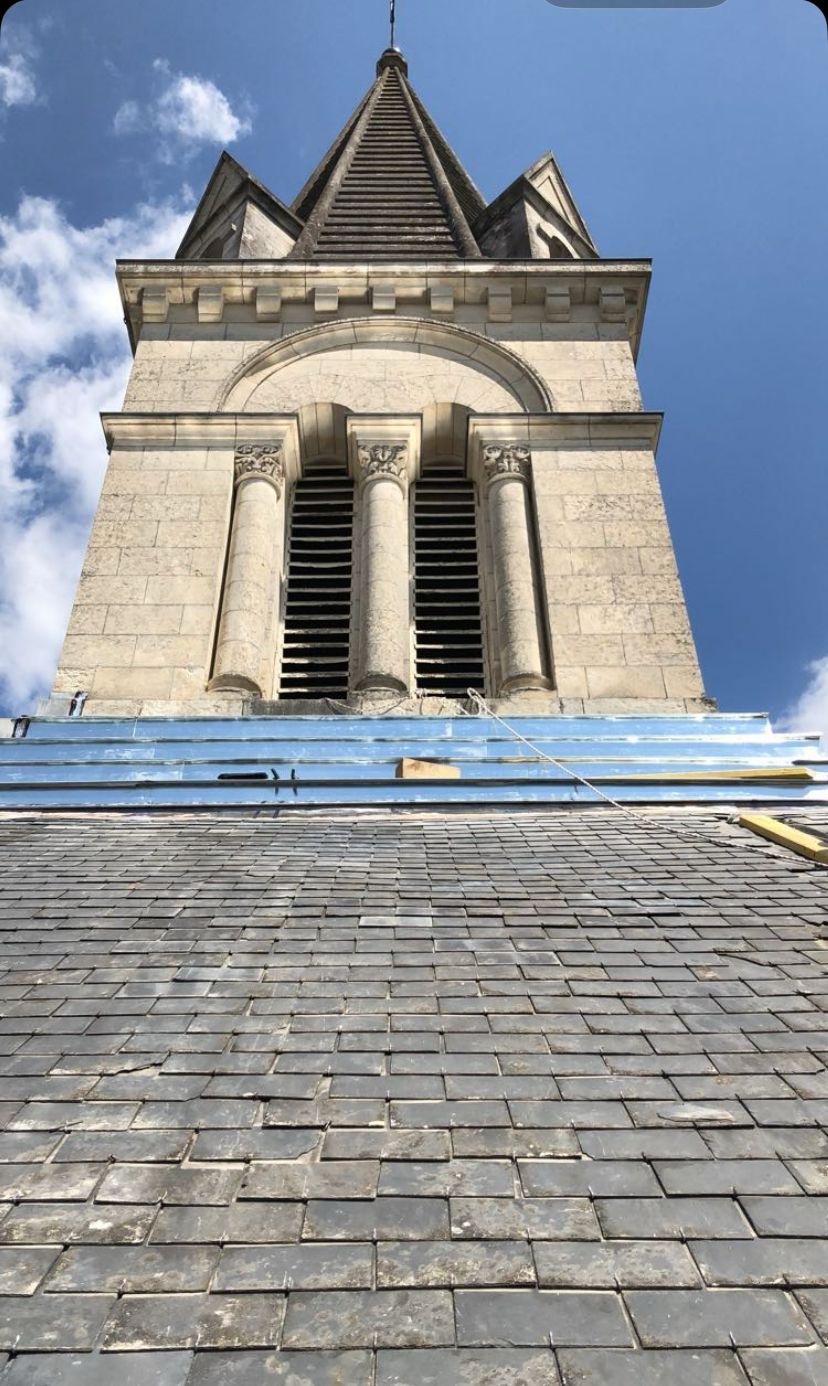 Vue en contre-plongée d'un clocher en pierre avec un toit d'ardoise et un ciel bleu au-dessus