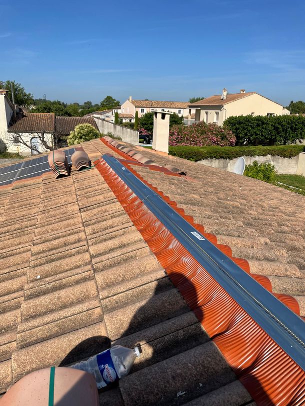 Travaux de toiture sur un toit en tuiles avec un filet de sécurité orange sous un ciel bleu dégagé