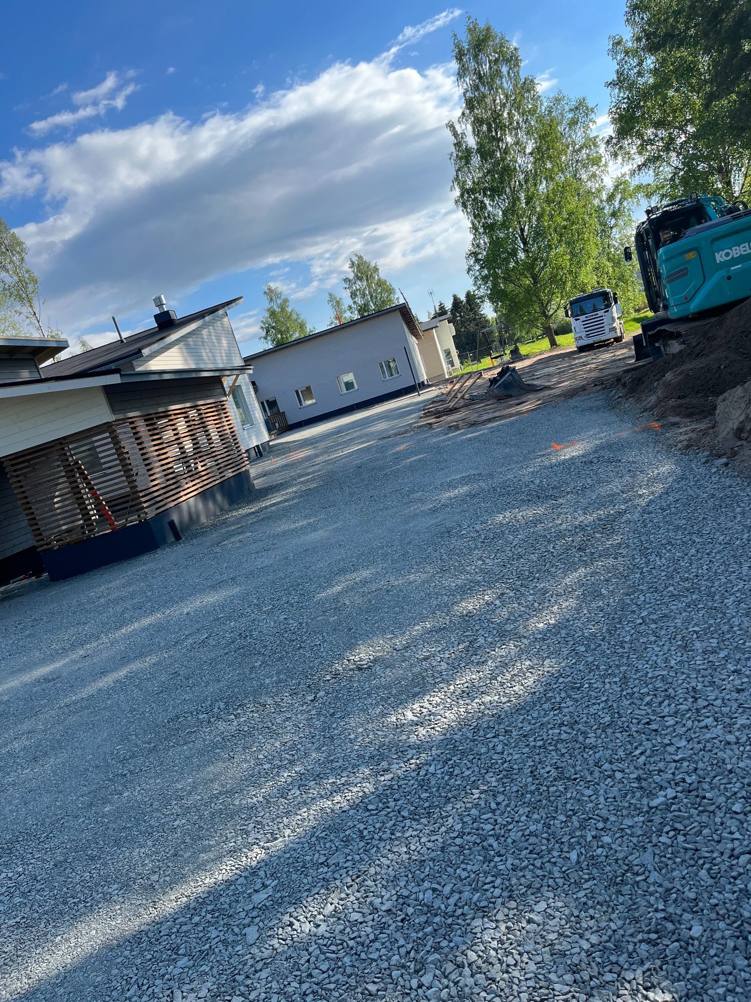Soratie talon ja puiden vieressä sinisen taivaan ja pilvien alla, rakennuskoneet oikealla