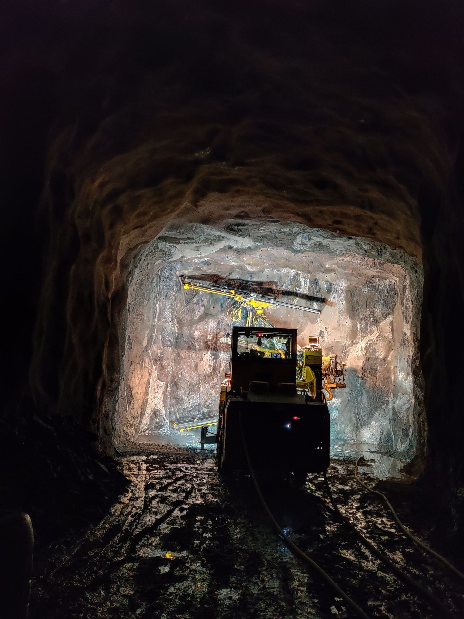 Pieni kaivosajoneuvo hämärässä tunnelissa, edessään kirkas aukko.