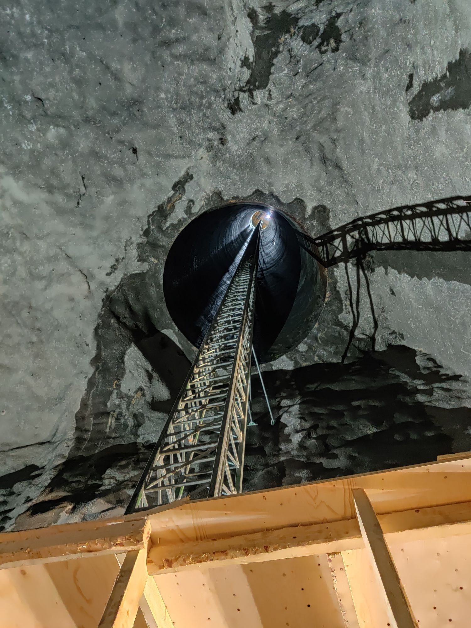 Korkea metallinen torni luolan sisällä, valaistu alhaalta päin, ja suuri tumma pallo lähellä kattoa.