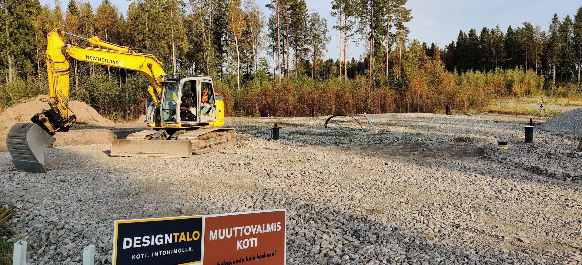 Keltainen kaivinkone työskentelee soratyömaalla metsäpuiden taustalla