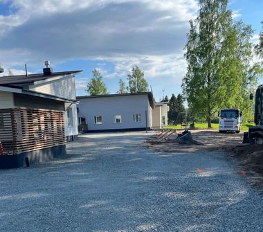 Moderni valkoinen talo mustilla yksityiskohdilla ja puisella terassilla, sininen taivas yläpuolella.