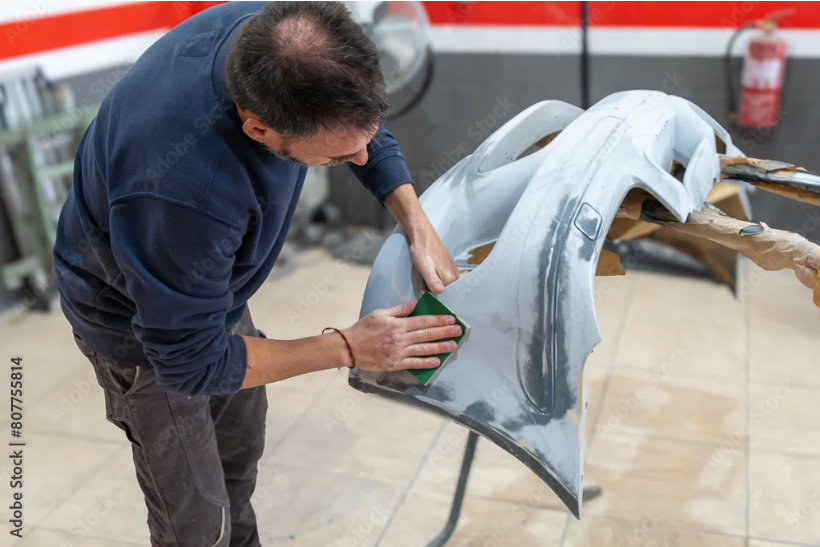 Hände montieren eine schwarze Stoßstange an einem teilweise braunen Fahrzeug.