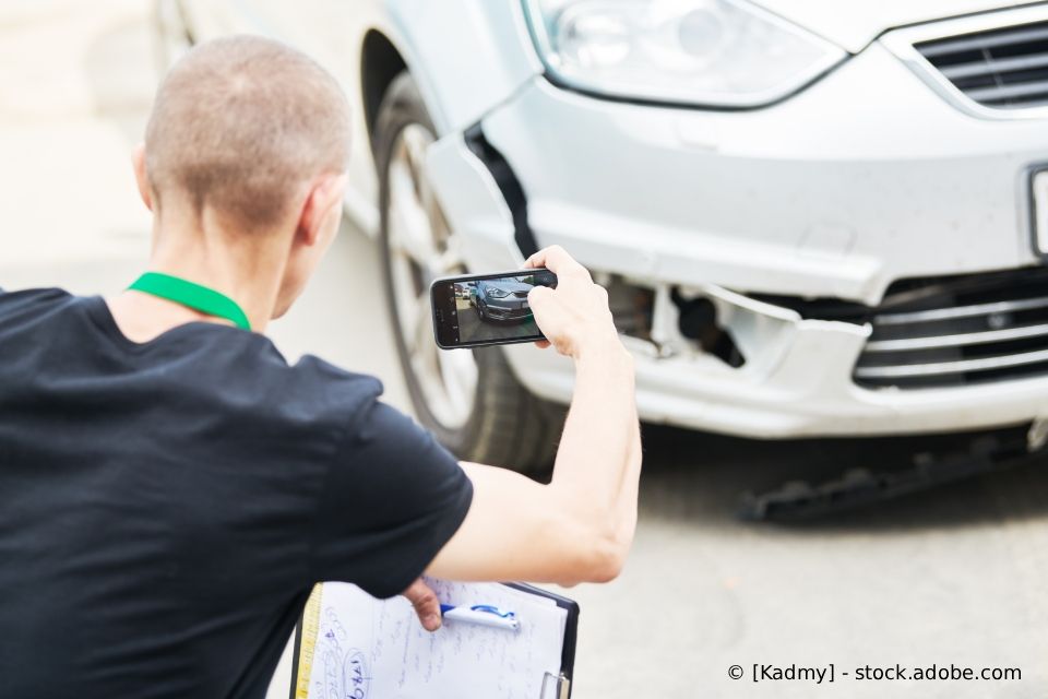 Eine Person fotografiert eine beschädigte Stoßstange, vermutlich für Versicherungszwecke.