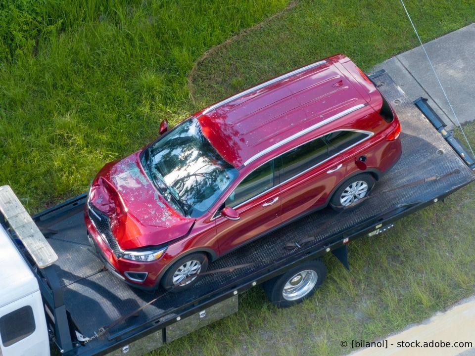 Ein roter Geländewagen mit Frontschaden steht auf einem Abschleppwagen, der auf einer Rasenfläche geparkt ist.