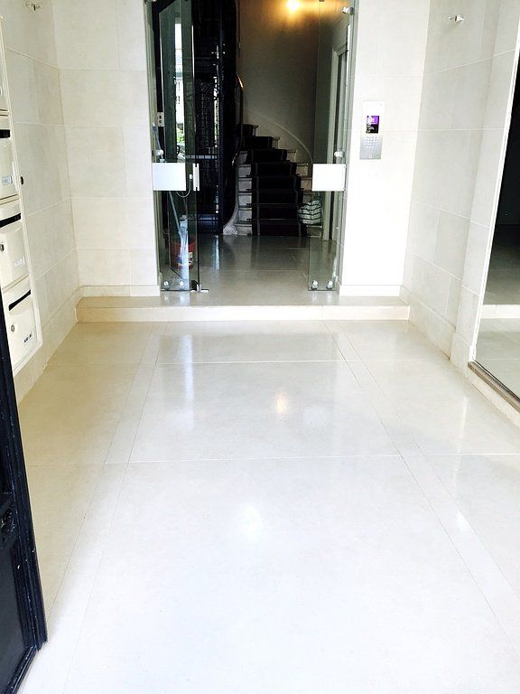 Entrée d'immeuble avec sol en carrelage blanc, escalier et ascenseur 