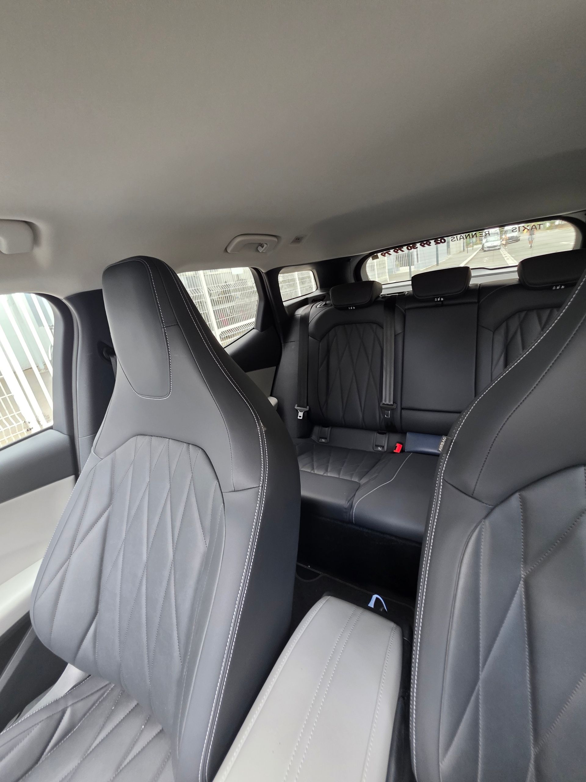 Intérieur de voiture avec sièges en cuir noir et accoudoir central rabattable, vu depuis la banquette arrière.