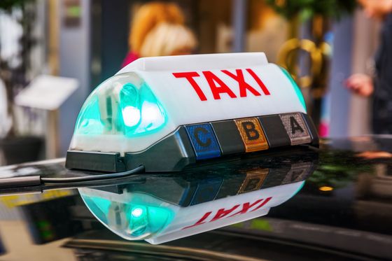 Panneau lumineux sur le toit d'un taxi, se reflétant sur le capot d'une voiture.
