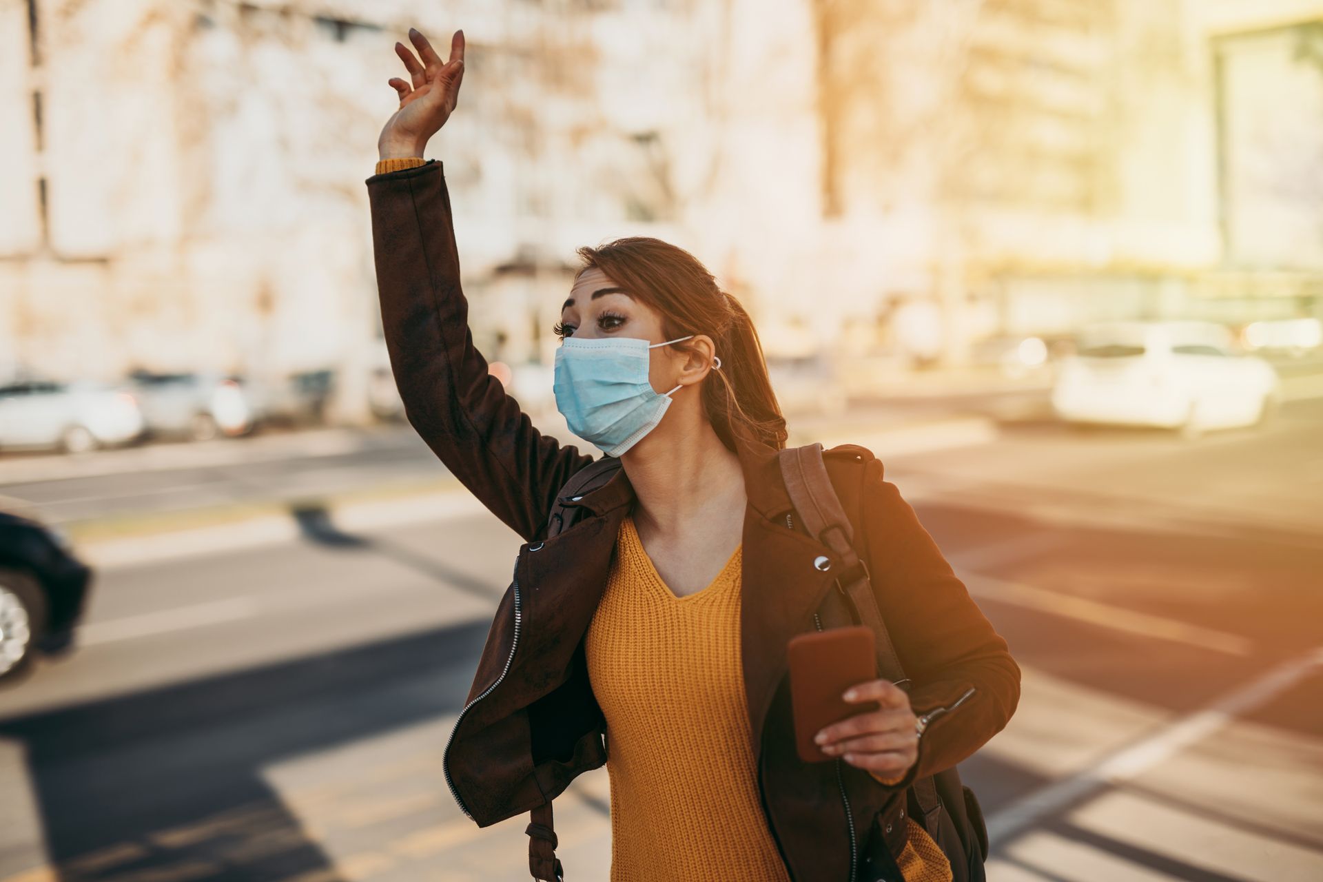 Une cliente avec un masque chirurgical hèle un taxi dans une rue ensoleillée.