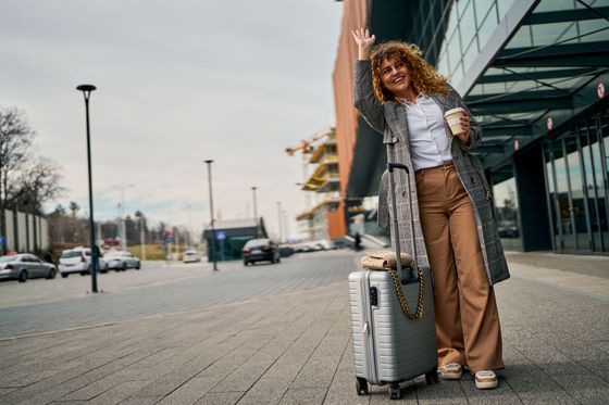 Voyageuse debout avec une valise devant un immeuble moderne dans une rue de la ville