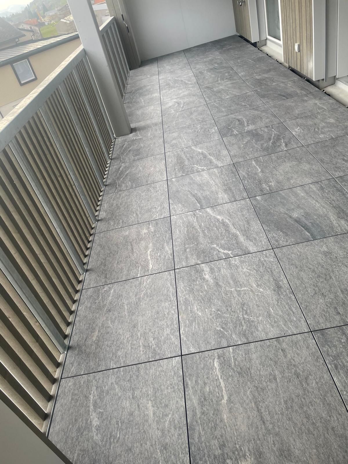 Eine Person mit gelben Handschuhen verlegt mit einem Gummihammer mehrfarbige Pflastersteine auf einem sandigen Untergrund.