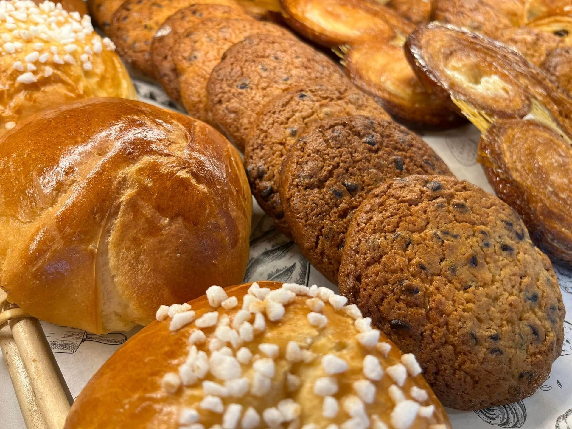 Assortiment de viennoiseries sur un plateau, comprenant des brioches brillantes et des pains aux graines.