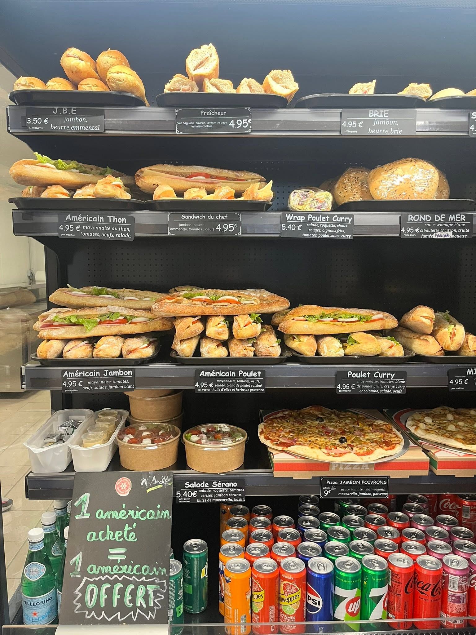 Présentoir de boulangerie avec assortiment de pains, viennoiseries, sandwichs et boissons en bouteille colorées sur des étagères noires