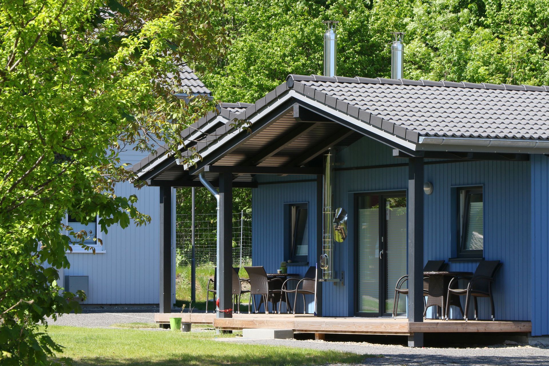 Moderne blaue Hütte mit Veranda unter grünen Bäumen an einem sonnigen Tag