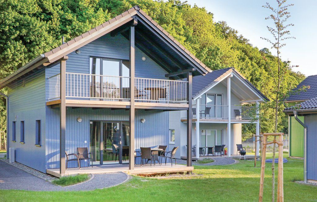Modernes graues Haus mit Balkonen und einem grünen Rasen, umgeben von Bäumen an einem sonnigen Tag