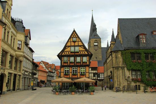 Historischer europäischer Marktplatz mit Fachwerkhäusern und einem Kirchturm vor bewölktem Himmel