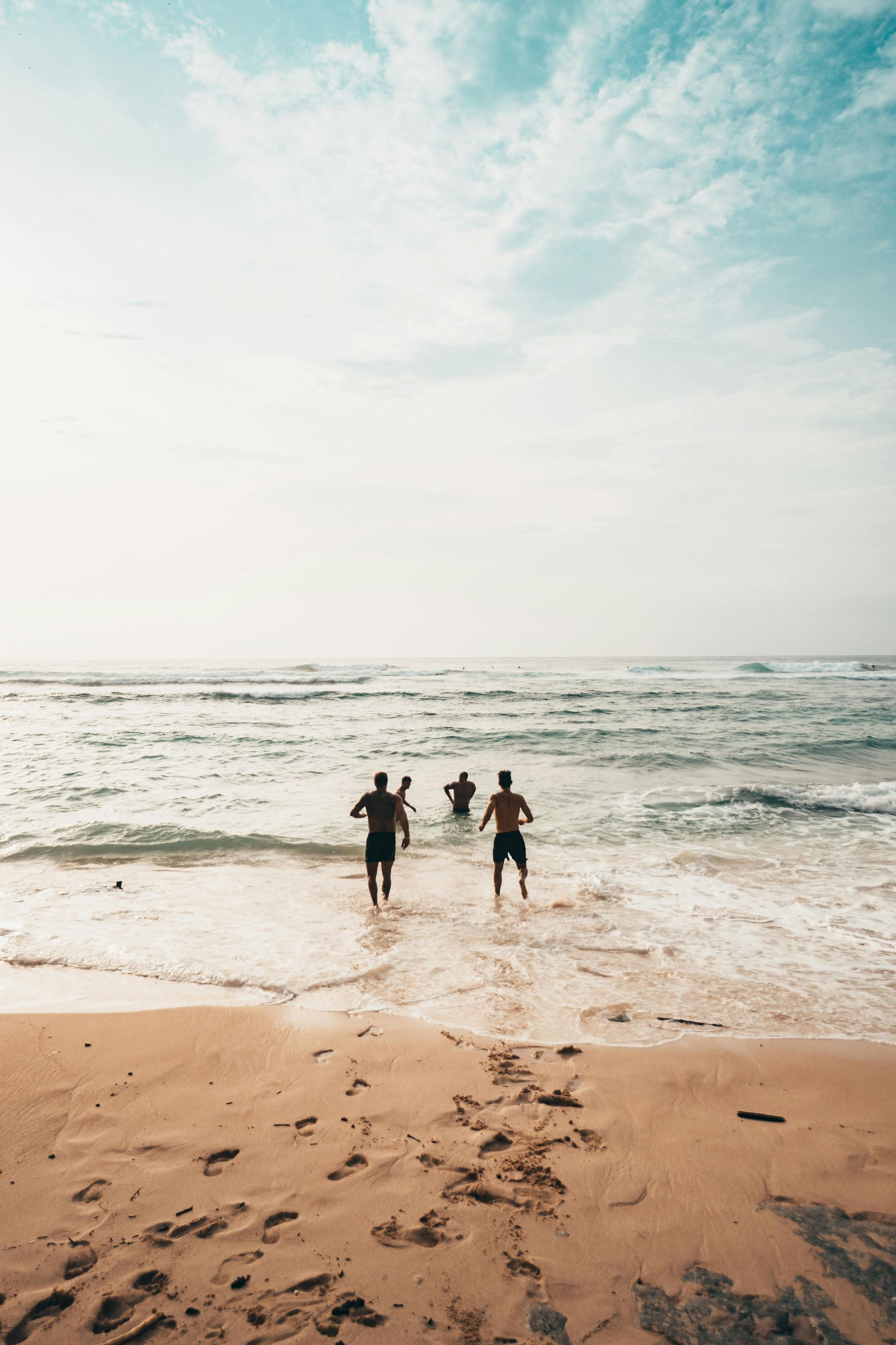 Drei Menschen laufen von einem Sandstrand aus unter einem strahlend blauen Himmel ins Meer.