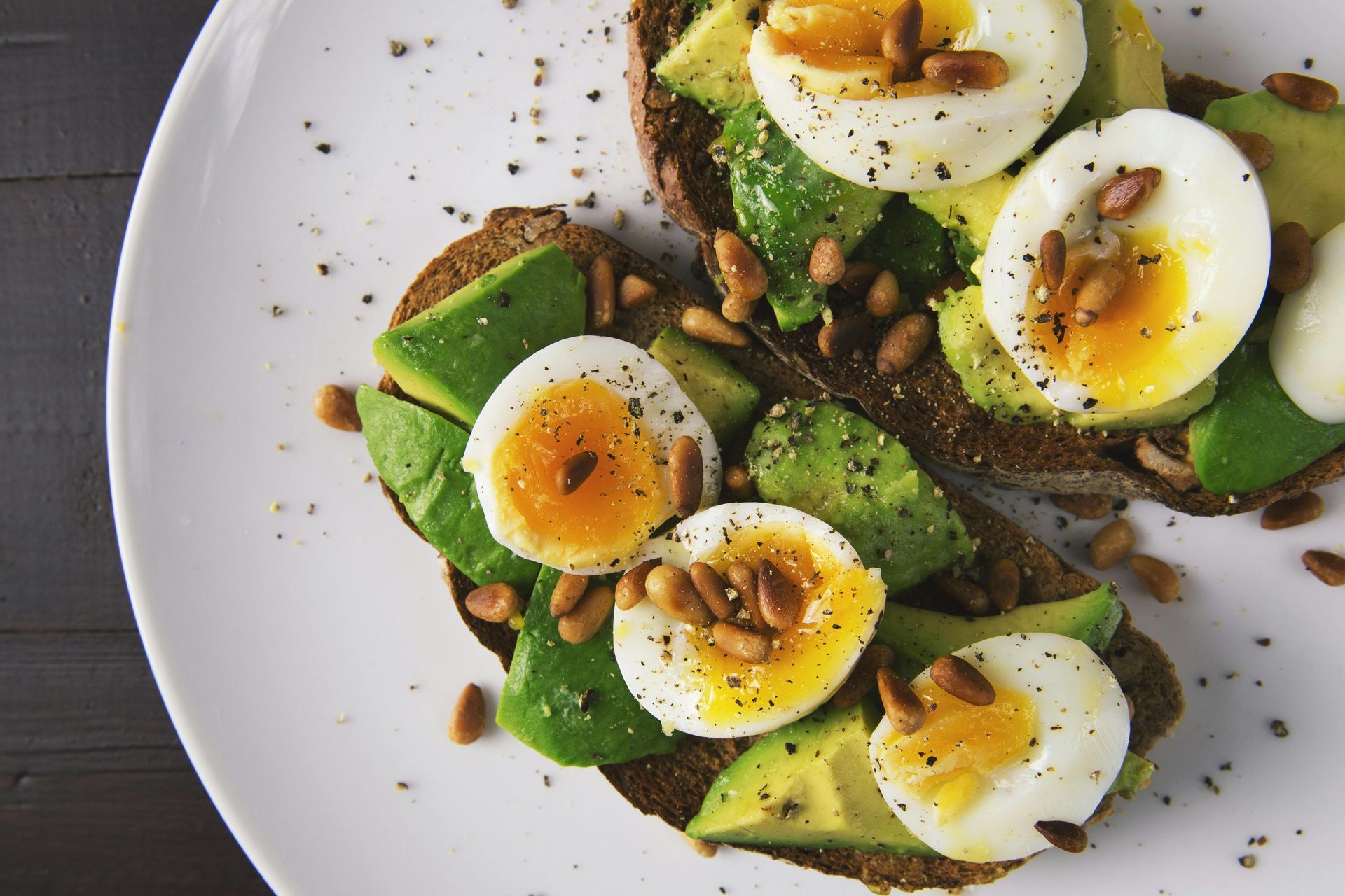 Avocado-Toast mit in Scheiben geschnittenen gekochten Eiern und Saaten auf einem weißen Teller